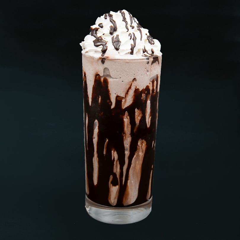A tall glass of chocolate milkshake with whipped cream and chocolate syrup drizzle.