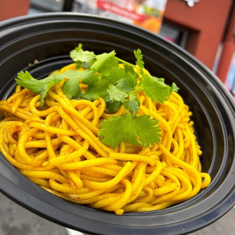 Bright yellow noodles with fresh cilantro in a black takeout bowl from Veo Cafe.