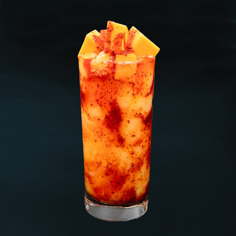 Veo Cafe's mango drink with chili powder and fresh mango chunks on a dark background.
