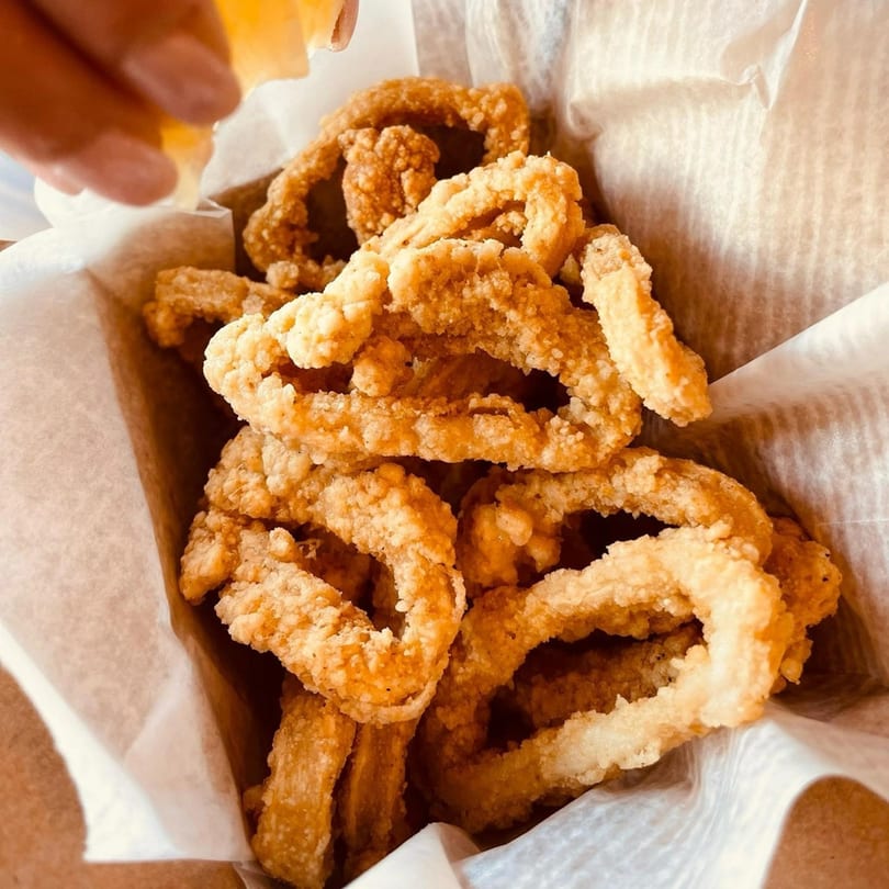 Golden-brown fried calamari rings in a paper-lined basket, with a hand squeezing lemon over them.