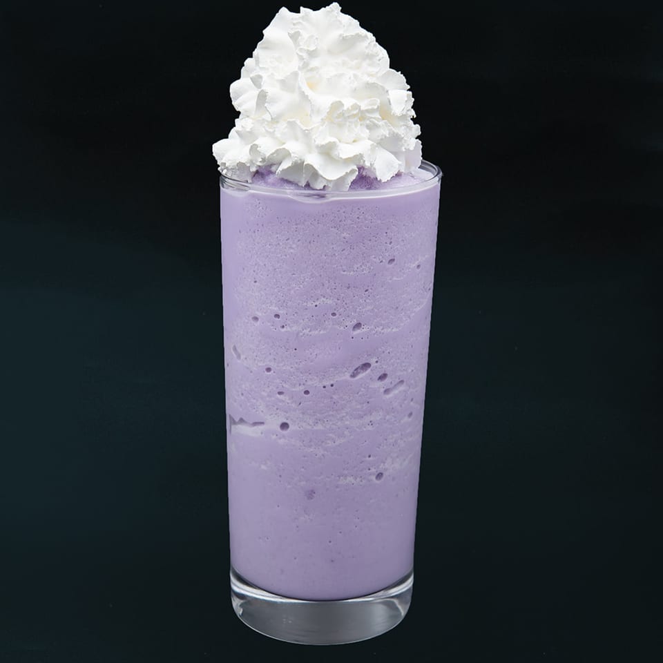 Tall glass of purple ube smoothie topped with a generous swirl of white whipped cream.