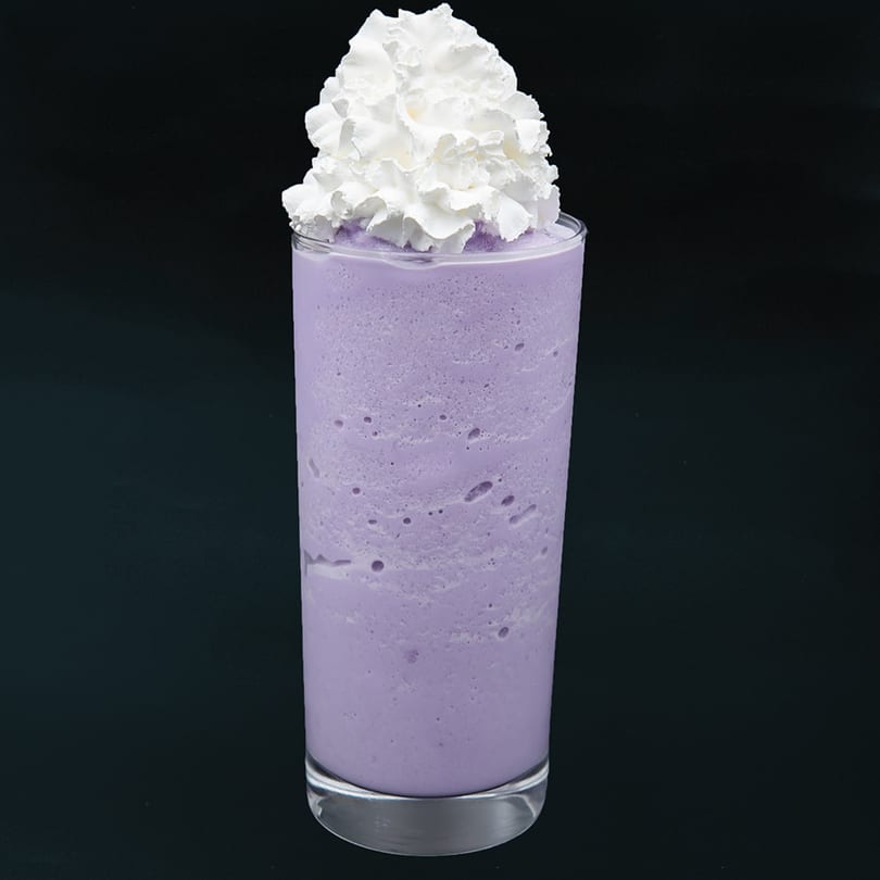 Tall glass of purple ube smoothie topped with a generous swirl of white whipped cream.