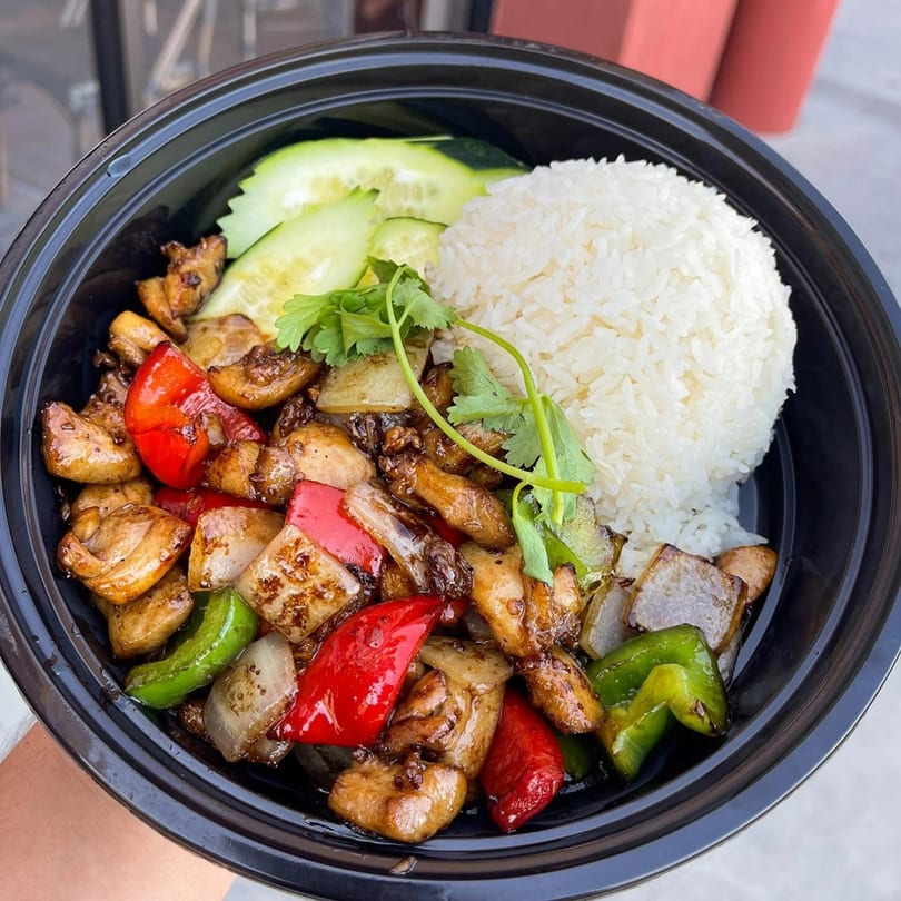 Veo Cafe's Asian-fusion chicken stir-fry with bell peppers, onions, white rice, and cucumber slices.